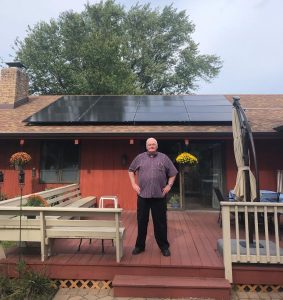 CUB group buy program participant Ken stands on the porch in front of his rooftop solar array.
