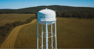 Water tower in green field behind mountain